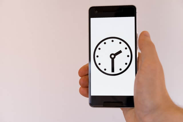 A hand holding a smartphone with a digital clock ticking on it. It’s the ability to save time and money that is one of the biggest benefits of unit testing.
